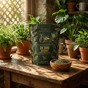 De Oro Reserve tea package on a rustic table surrounded by green plants
